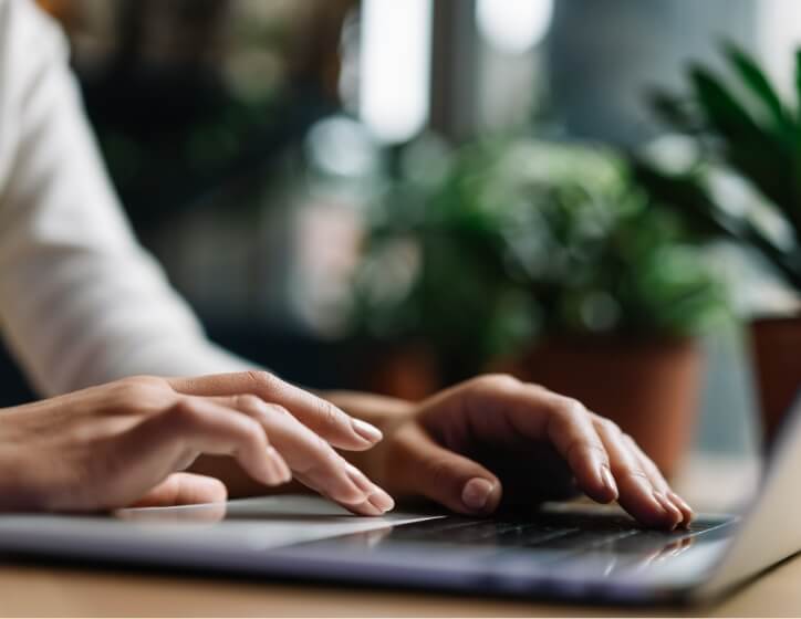 A person focused on typing on a laptop computer, with hands positioned on the keyboard and a screen illuminated.