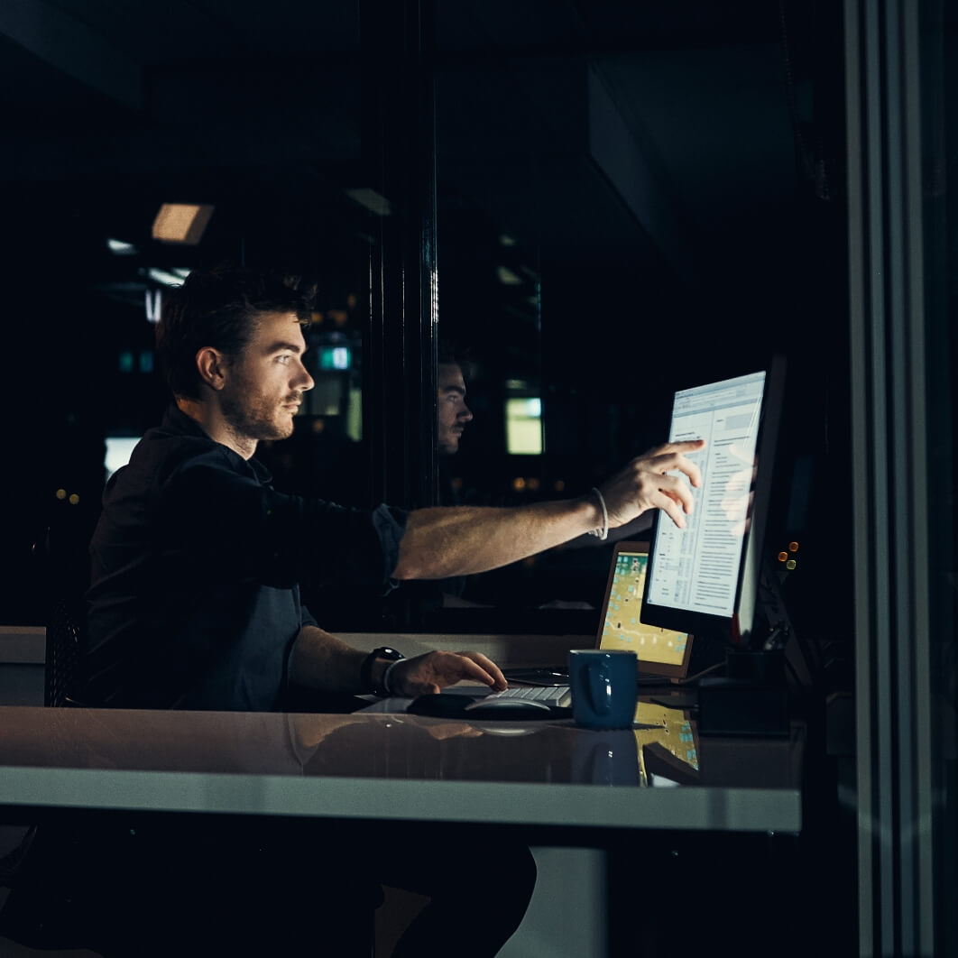 Focused professional working late at night, analyzing data on a computer in a modern office setting.