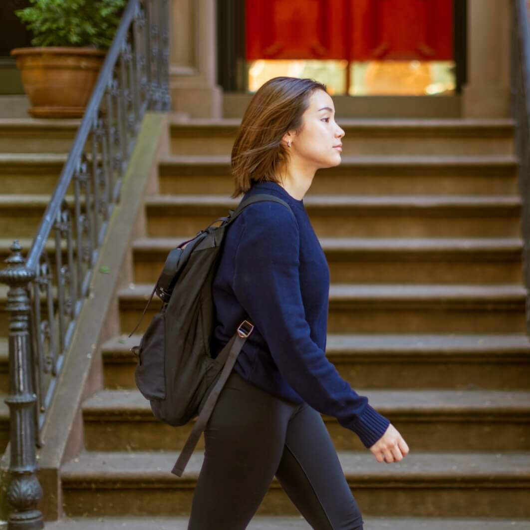 A woman with a backpack walks down a flight of stairs, illustrating a moment of daily life and activity.